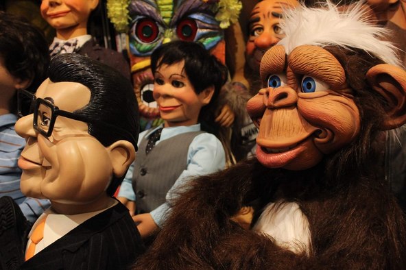 A close group of ventriloquial figures including a man in glasses, a boy figure and a monkey