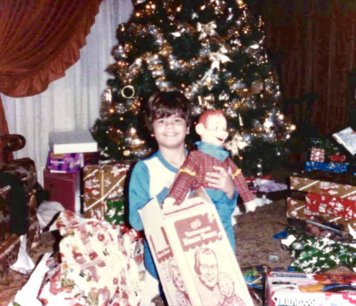 A boy on Christmas morning holding a boxed Howdy Doody ventriloquist figure